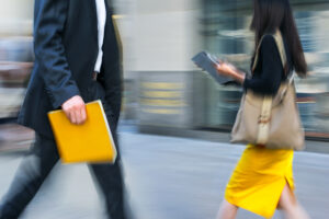 Business professionals walking through a financial district, one carrying a yellow folder.